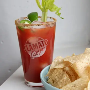 A tall glass of red tomato-clam cocktail with a celery stalk and a salted rim.