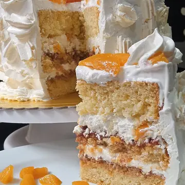 A tall slice of layered sponge cake with cream, peaches and crumbled meringue.