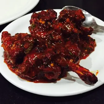 Glossy, dark red, sticky battered chicken pieces on a white plate.