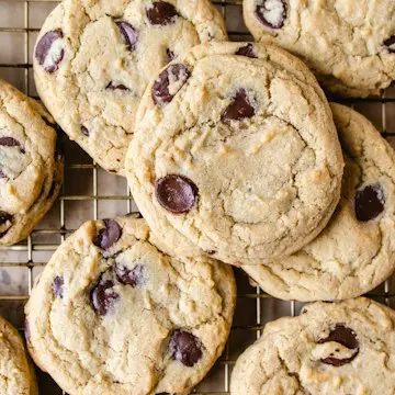 A heap of chocolate chip cookies on a cooling rack.