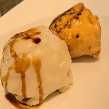 Two chunky dumplings, one fried and one steamed, drizzled with soy sauce.