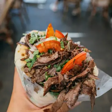 A flatbread stuffed with sliced spit-roasted meat, salad and sauce, held in a hand.