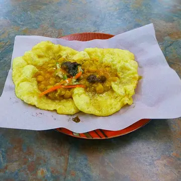 Two soft fried flatbreads topped with curried chickpeas and chutneys on paper.