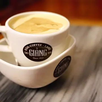 A small cup of coffee topped with a thick, pale yellow layer of whipped egg cream.