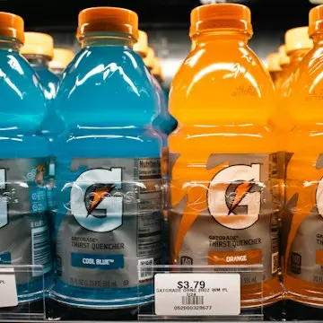 Rows of blue and orange sports-drink bottles on a shop shelf.