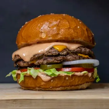 A tall burger with a beef patty, melted cheese, lettuce and tomato in a glossy bun.
