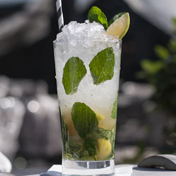 A tall glass of crushed ice, lime and mint leaves with a straw.