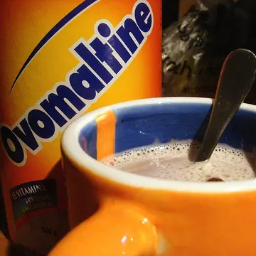 A mug of hot malted chocolate drink in front of a tin of the powder.
