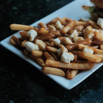 French fries scattered with white cheese curds on a white plate.