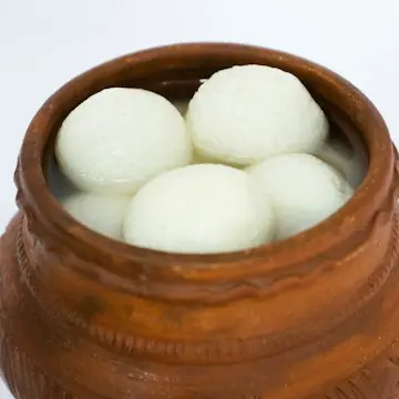 White, spongy cheese balls in syrup in a clay pot.