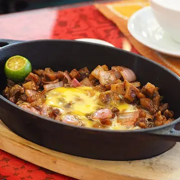 A sizzling iron plate of chopped crispy pork with an egg and chilli.