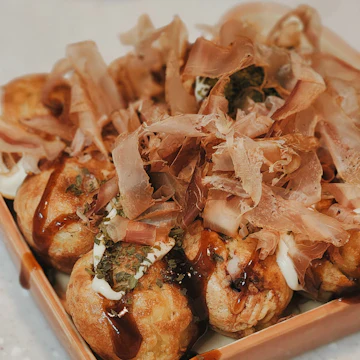 Round, golden batter balls with brown sauce and mayonnaise, topped with curling flakes of dried fish.